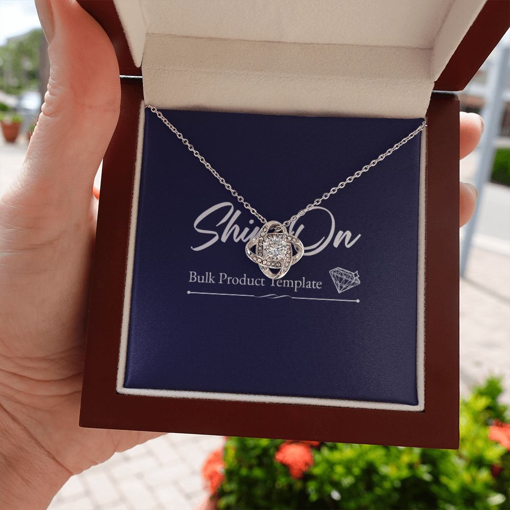 A hand holds a wooden box and knot necklace on a message card